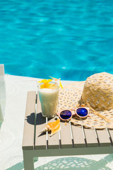 Swimming pool table with sunglasses, hat and fresh cocktail