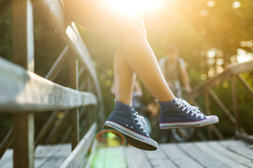 Young woman sitting on a bridge railing in jeans sneakers - Powered by Adobe