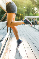 Young woman sitting on a bridge railing in jeans sneakers - obrazy, fototapety, plakaty