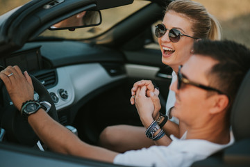 cheerful family couple lovers smiling and cheating to each other driving a cabriolet and searching the location they need by pointing on car gps system
