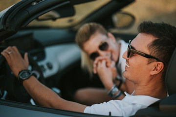 cheerful family couple lovers smiling and cheating to each other driving a cabriolet and searching the location they need by pointing on car gps system