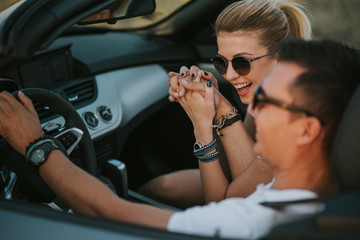 cheerful family couple lovers smiling and cheating to each other driving a cabriolet and searching the location they need by pointing on car gps system
