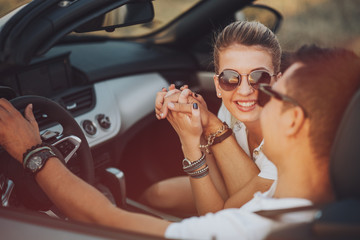 cheerful family couple lovers smiling and cheating to each other driving a cabriolet and searching the location they need by pointing on car gps system
