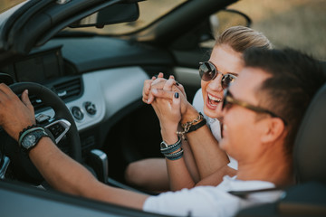 cheerful family couple lovers smiling and cheating to each other driving a cabriolet and searching the location they need by pointing on car gps system