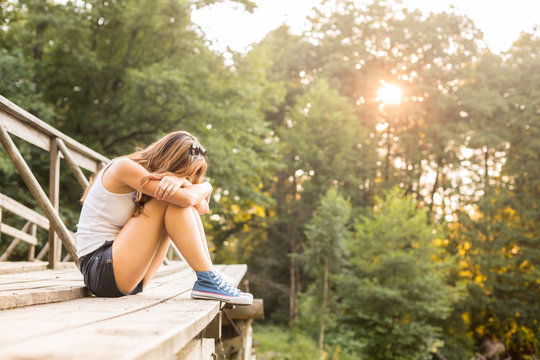 Young woman resting on a wooden bridge in jeans sneakers
