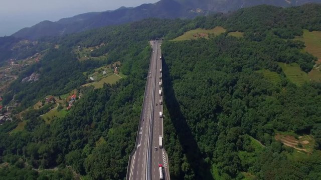 Highway bridge mountain viaduct road aerial 4k above top view. Cars lorry truck traffic Europe cargo freight logistics. Vehicles move on massive bridge overpass above green forest valley in Italy Alps
