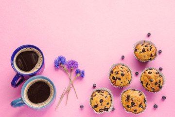 Blueberry muffins, two cups of coffee and cornflowers on pink ba