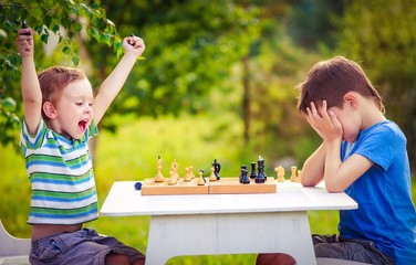 vivid emotions after the game of chess. two young chess players outdoors. boy rejoices won a game...