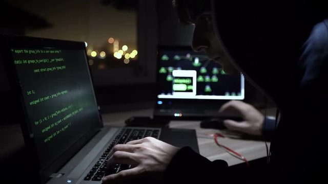Hacker in hooded jacket using computer at table