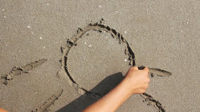 Woman draws a sun on the wet beach sand.