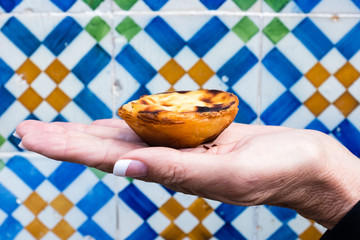 Portuguese custard tart from patisserie in Belem, Lisbon (Portugal) held against wall with...