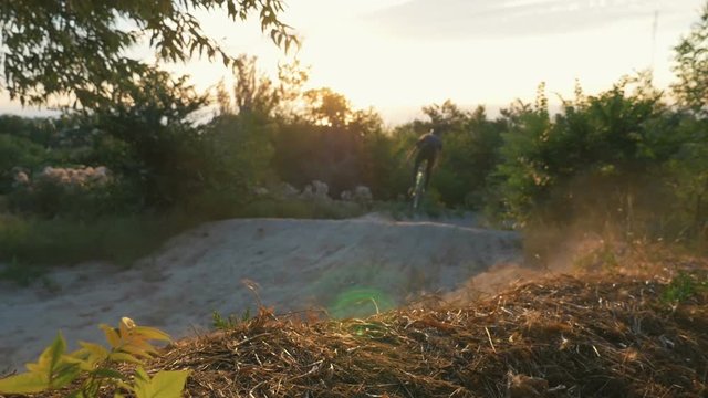 A mountain biker riding a track downhill at sunrise or sunset, dolly shot