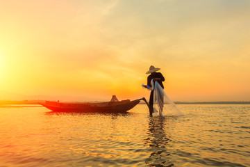 Silhouette of asian fisherman on wooden boat ,fisherman in action throwing a net for catching...