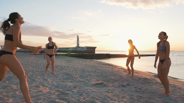 Group of young girls playing beach volleyball during sunset or sunrise, slow motion