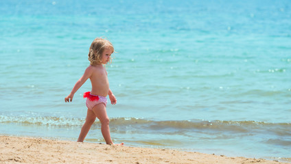 Little girl baby walking on sandy seashore