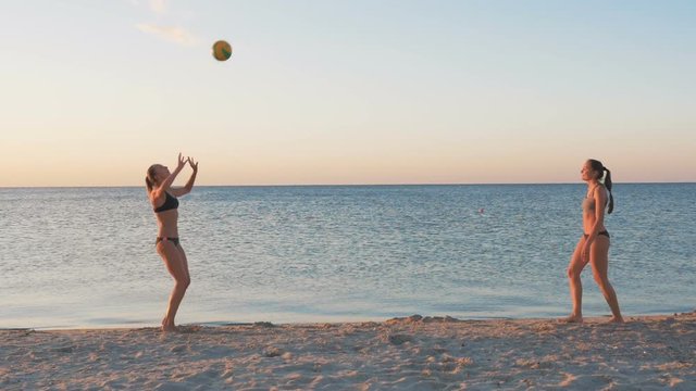 Two young girls playing beach volleyball during sunset or sunrise, slow motion