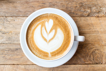 Cup of coffee with heart pattern in a white cup on wooden backgr