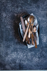 Close up of a variety of silverware over blue stone table.