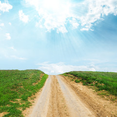 rural road in green grass to sun in blue sky