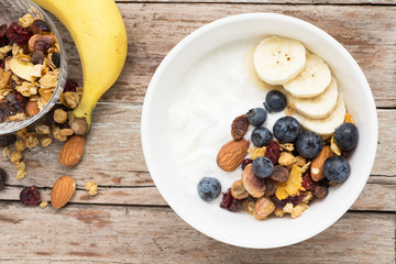 brunch : homemade yogurt with granola and banana in bowl on wooden table background.
