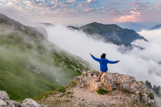 Young Woman Backpacker Hiking At Mountain Peak Above Clouds And Fog