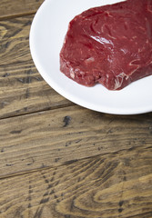 A cut of raw rump steak meat on a rustic wooden table top background forming a page border