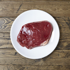 An aerial view of a cut of raw rump steak meat on a rustic wooden table top background