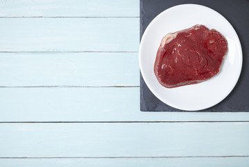 An aerial view of a fillet of rump steak meat on a painted wooden kitchen counter background forming a page border