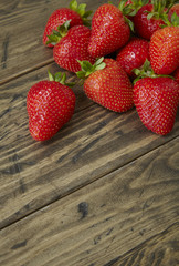 A pile of whole home grown strawberries on a rustic table top background forming a page border