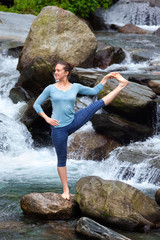 Woman doing Ashtanga Vinyasa Yoga asana outdoors at waterfall