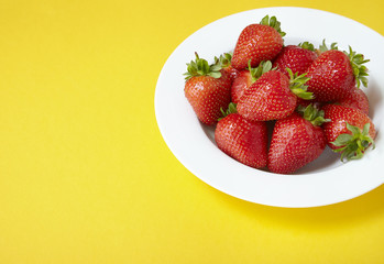 A bowl of whole ripe strawberries on a bright yellow background forming a page border
