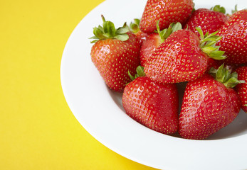 A bowl of whole ripe strawberries on a bright yellow background