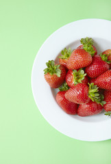 An aerial view of a bowl of whole ripe strawberries on a green background