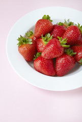 A bowl of fresh ripe strawberries on a pastel pink background