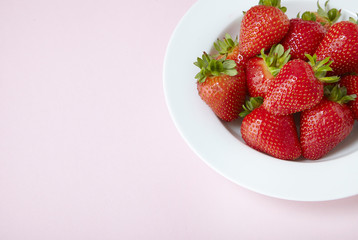 A bowl of whole ripe strawberries on a pastel pink background forming a page border