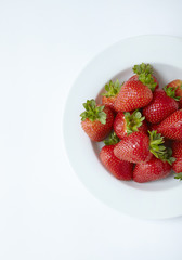 An aerial view of a bowl of whole ripe strawberries on an off white background