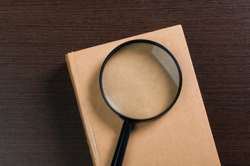 Magnifying glass and book o the wooden background