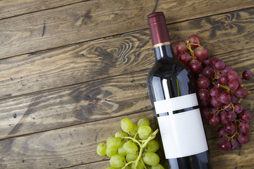 A bottle of red wine with bunches of grapes on a distressed wooden table top background, arranged...