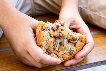 Child holding large half eaten homemade chocolate chip cookie.