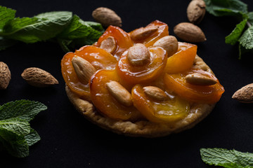 Pie with apricot. Traditional french tart with fruits on dark marble background. Decorated almonds and mint leafs. Delicious dessert with copy space closeup.
