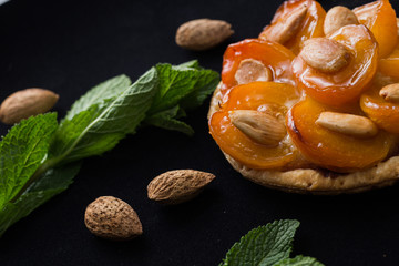 Pie with apricot. Traditional french tart with fruits on dark marble background. Decorated almonds and mint leafs. Delicious dessert with copy space closeup.

