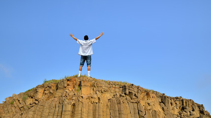 Man standing on cliff above blue sky
