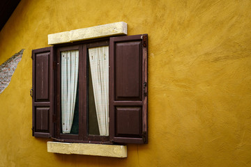 Wooden window with curtain on cracked yellow wall