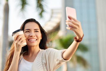 Smiling Vietnamese woman taking selfie with take-out coffee