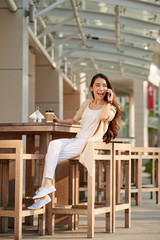 Young woman sitting in cafe and talking on phone with friend