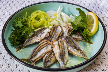 Cooked sardines with green salad in old-fashion plate on table