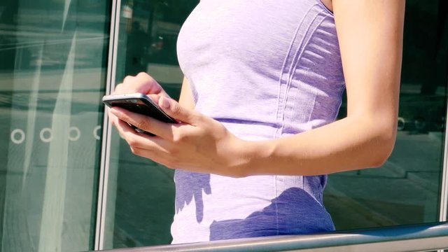On a sunny day a sportive woman edits her fitness app in front of a modern building.