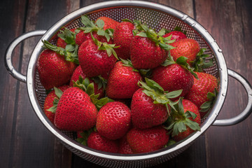 Fresh strawberries in stainless steel colander on a wood surface