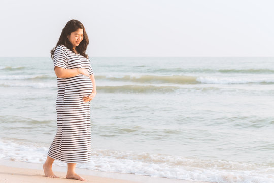 Pregnant woman holding her belly on the beach with copy space.