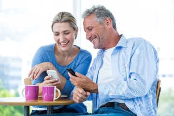Smiling couple using mobile phones at cafe